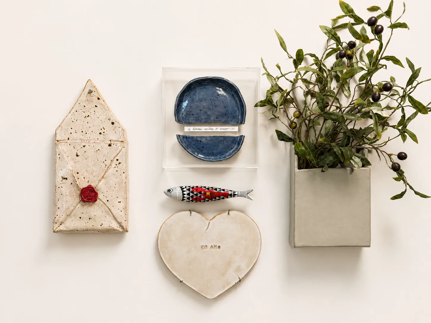 Composição de peças decorativas na parede, com envelope, pratos, peixe, coração e vaso com folhagens